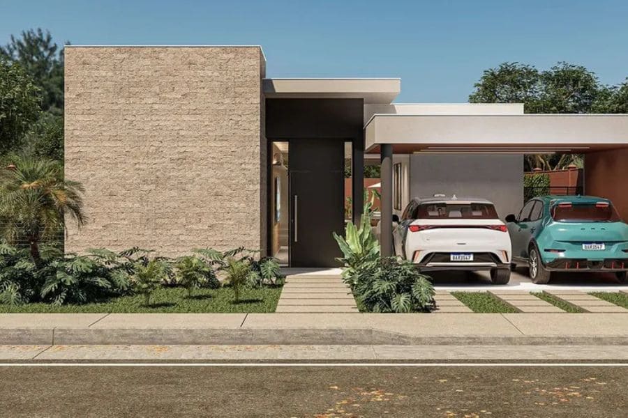 Imagem da fachada moderna de uma das Casas Le Jardin, com revestimento de tijolos claros, entrada principal, e uma garagem coberta (carport) com dois carros.