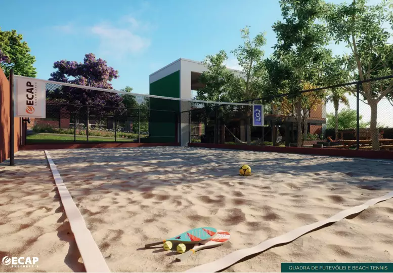 Imagem de uma quadra de areia para futevôlei e beach tennis do condomínio Le Grand Jardin, com rede, bola e raquetes, cercada por vegetação e com estruturas de lazer ao fundo.