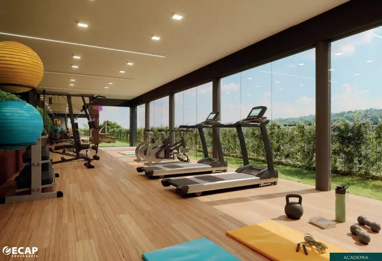 Imagem de uma academia moderna e bem equipada do condomínio Le Grand Jardin, com esteiras, bicicletas ergométricas, pesos e bolas de ginástica, além de uma grande parede de vidro com vista para a natureza.