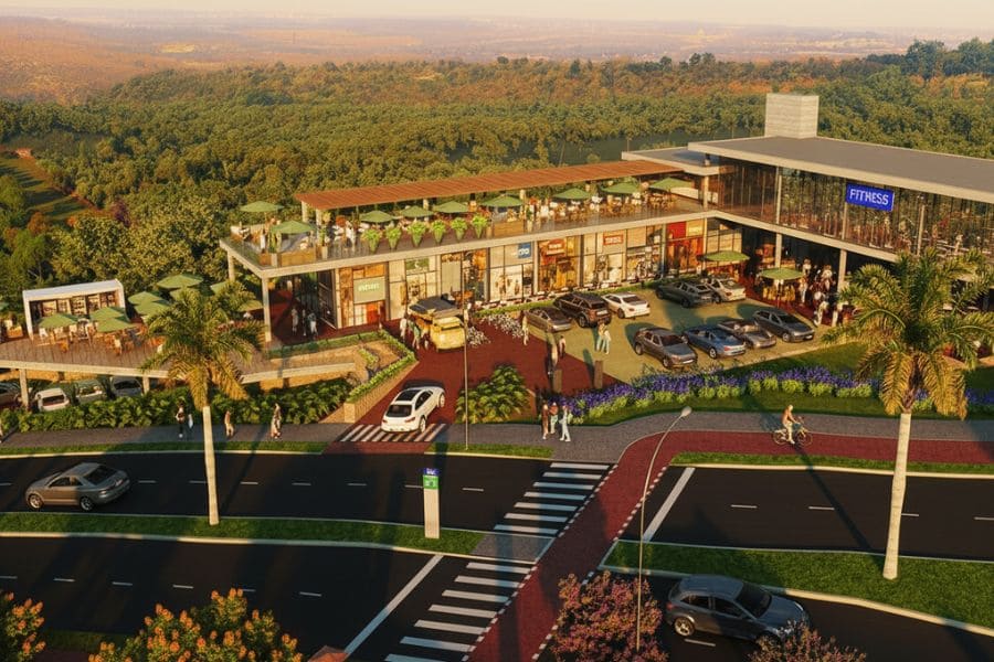 Vista aérea de um moderno centro comercial de dois andares, com lojas, estacionamento, área de alimentação e paisagismo, que atende ao complexo residencial Casas Le Jardin, cercado por uma vasta área verde.